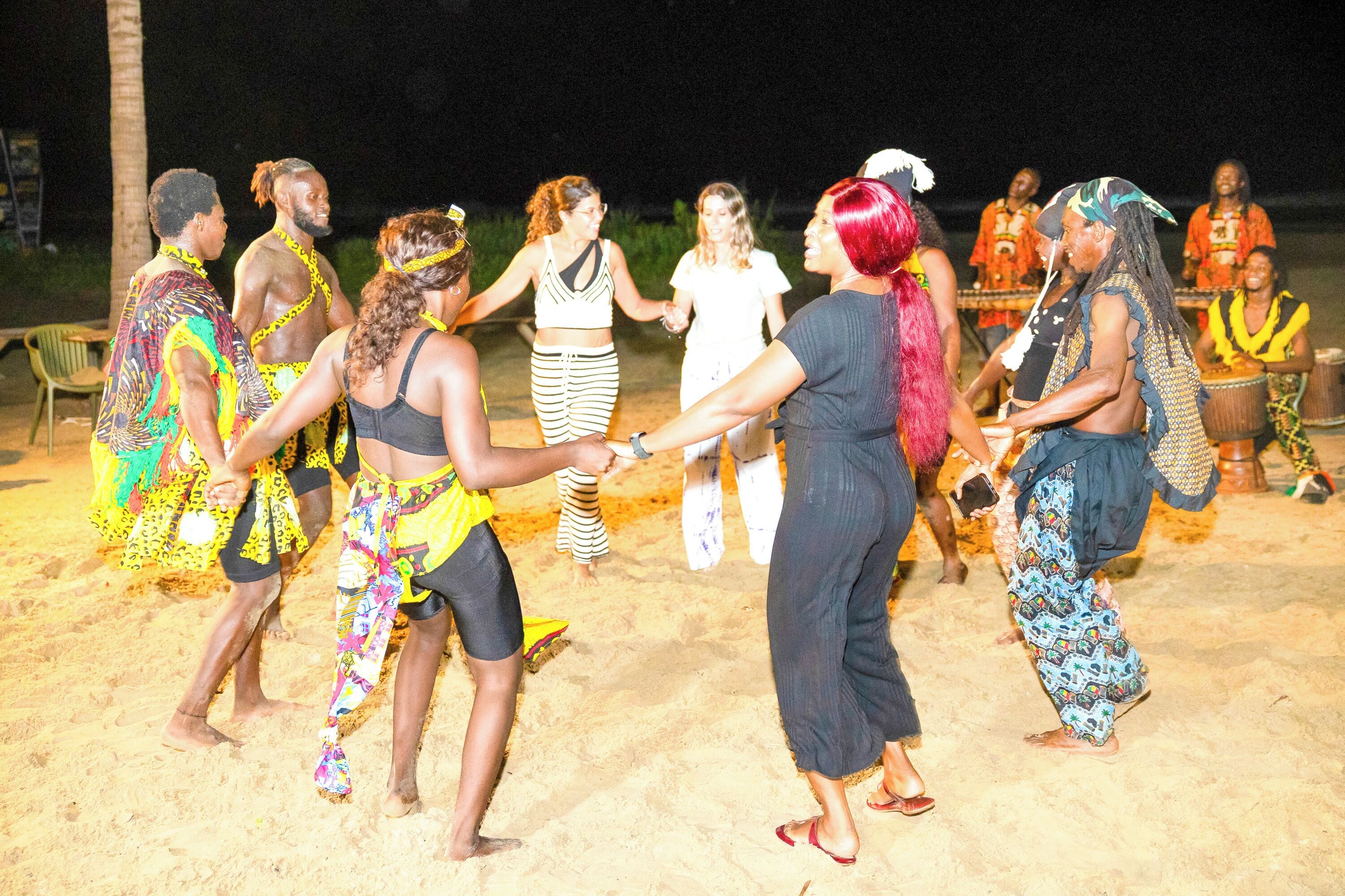 A group of people dancing on a sandy beach at night.
