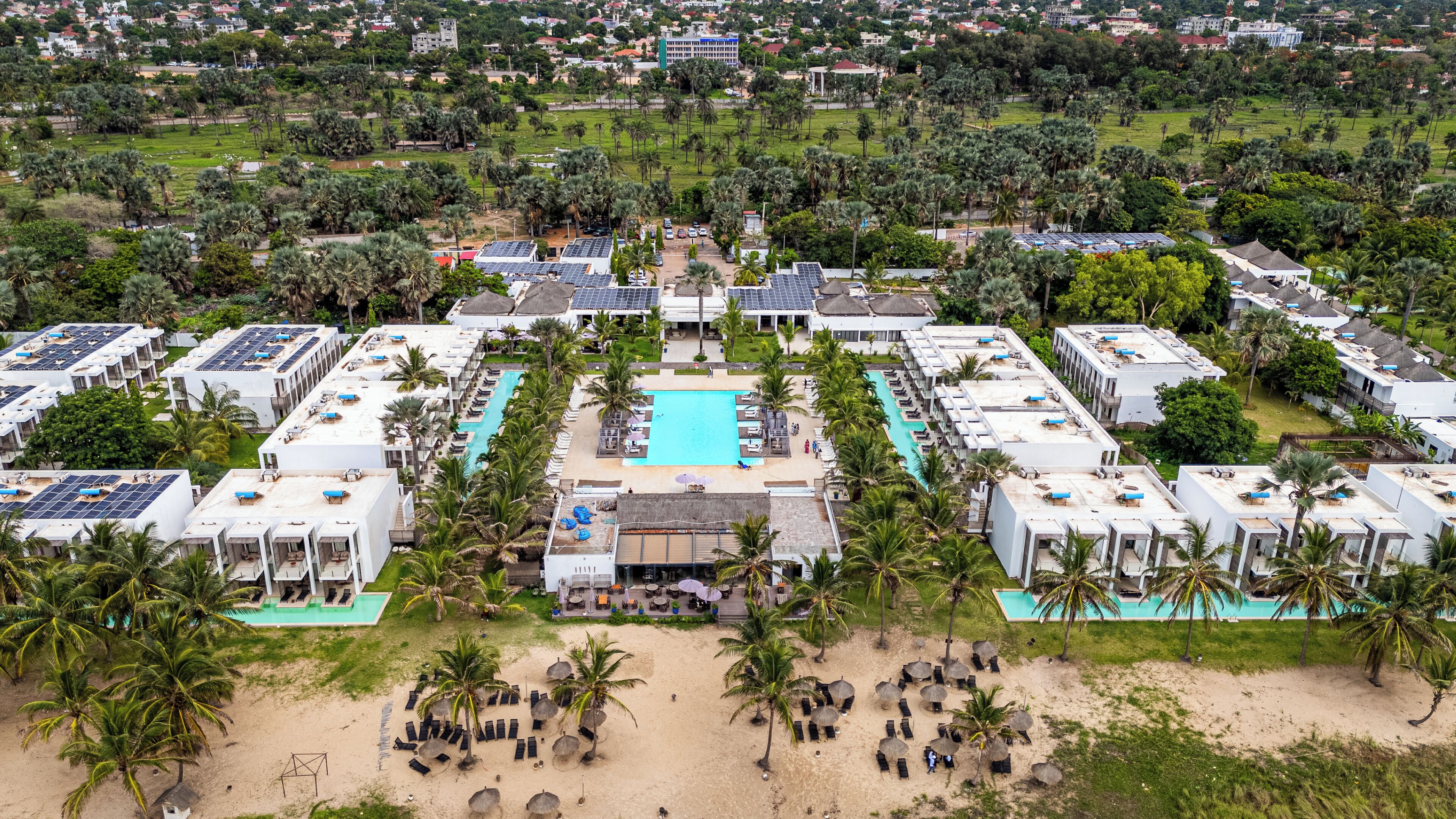 Un resort con varias edificaciones, una piscina central y palmeras aledañas.