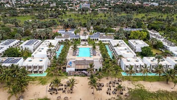 Un resort con varias edificaciones, una piscina central y palmeras aledañas.