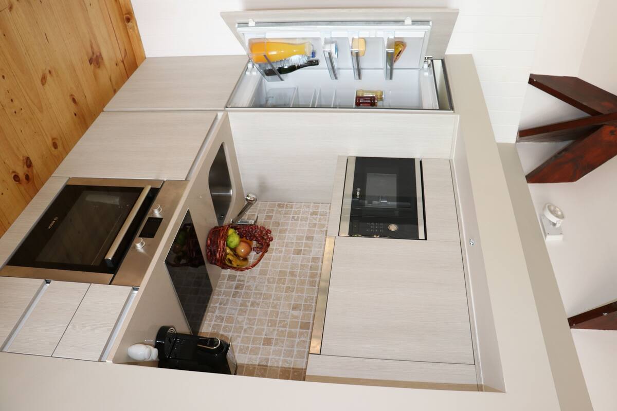 A compact kitchen with a microwave, oven, and a small sink. There is a basket with fruits on the counter.