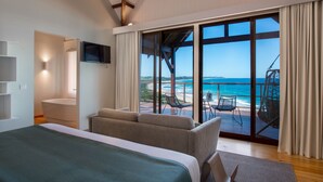 A modern hotel room with a large bed, a TV, and a balcony with ocean views.
