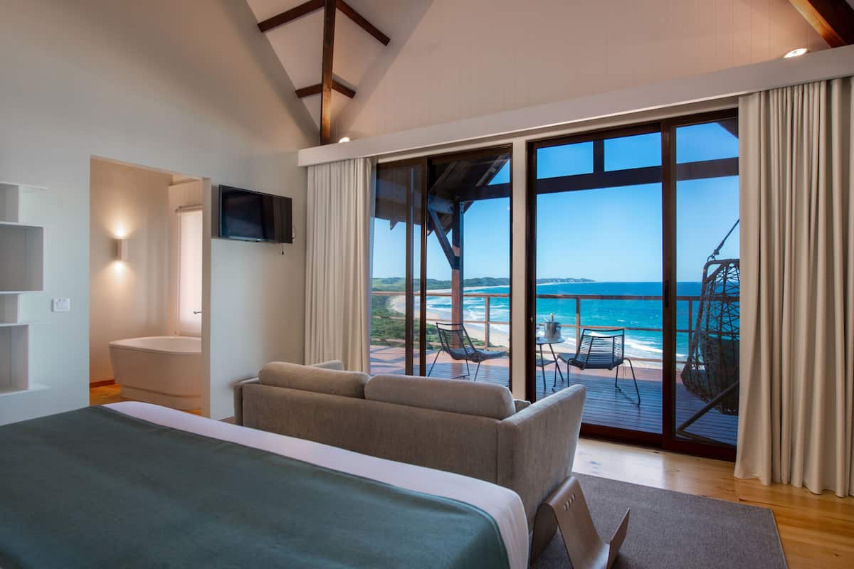 A modern hotel room with a large bed, a TV, and a balcony with ocean views.