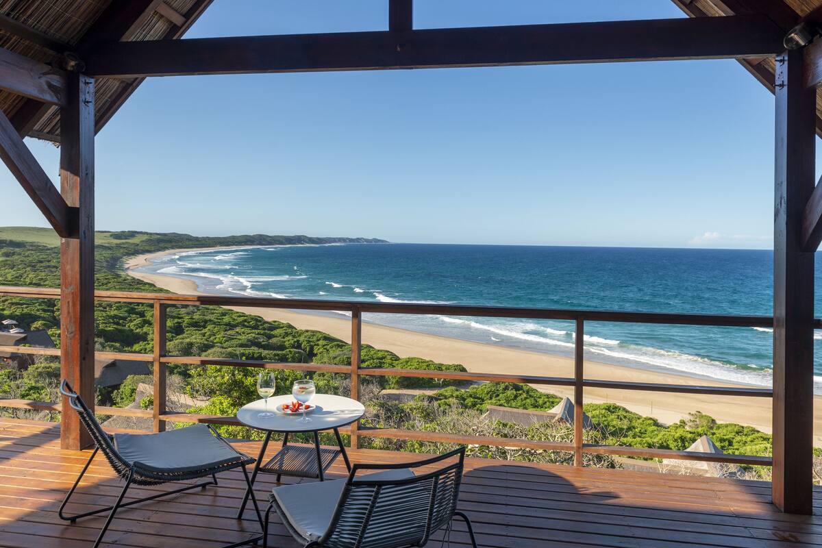 A wooden deck with a table and chairs overlooking a beach.