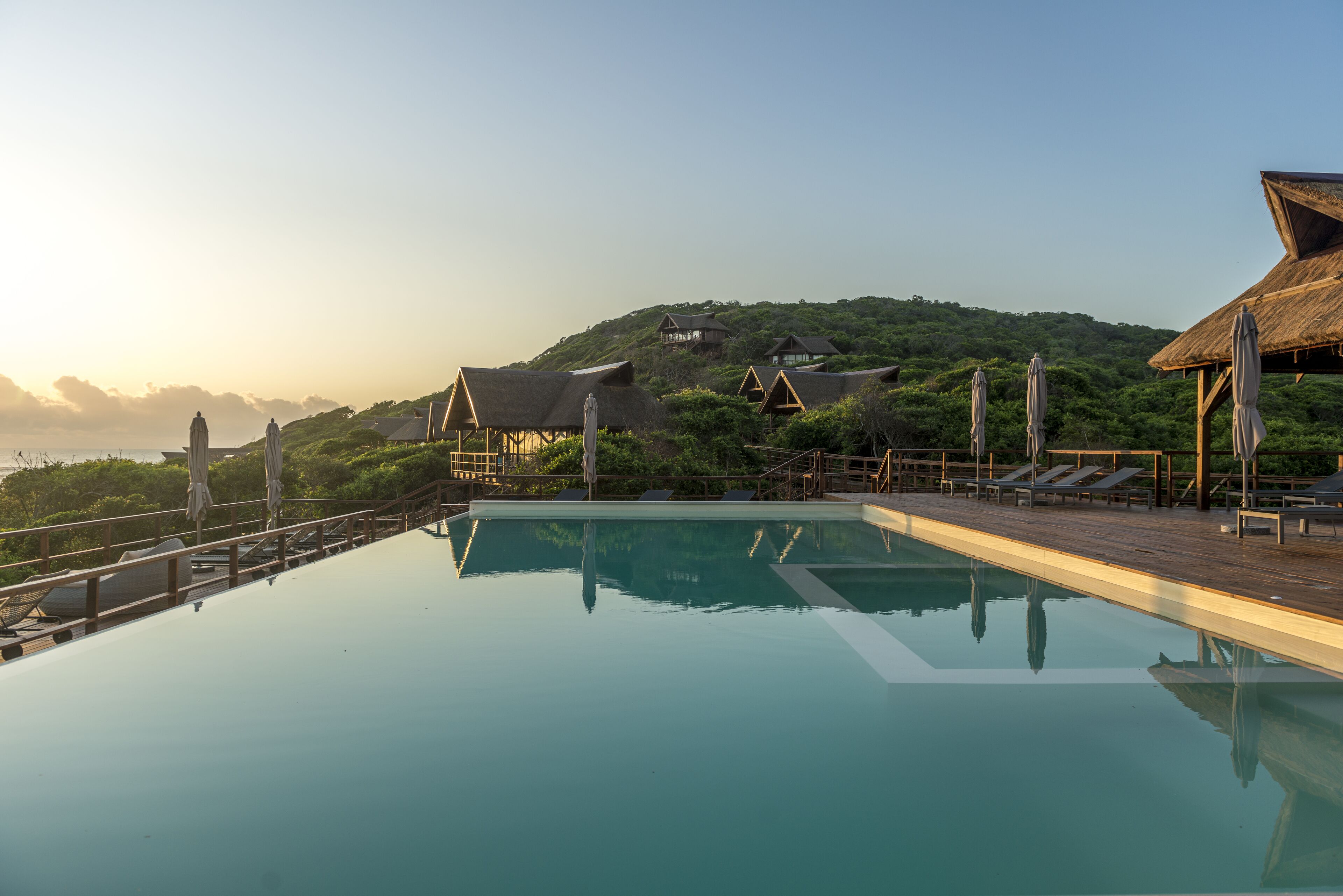 A swimming pool with lounge chairs and umbrellas, surrounded by wooden deck and overlooking a hilly landscape.