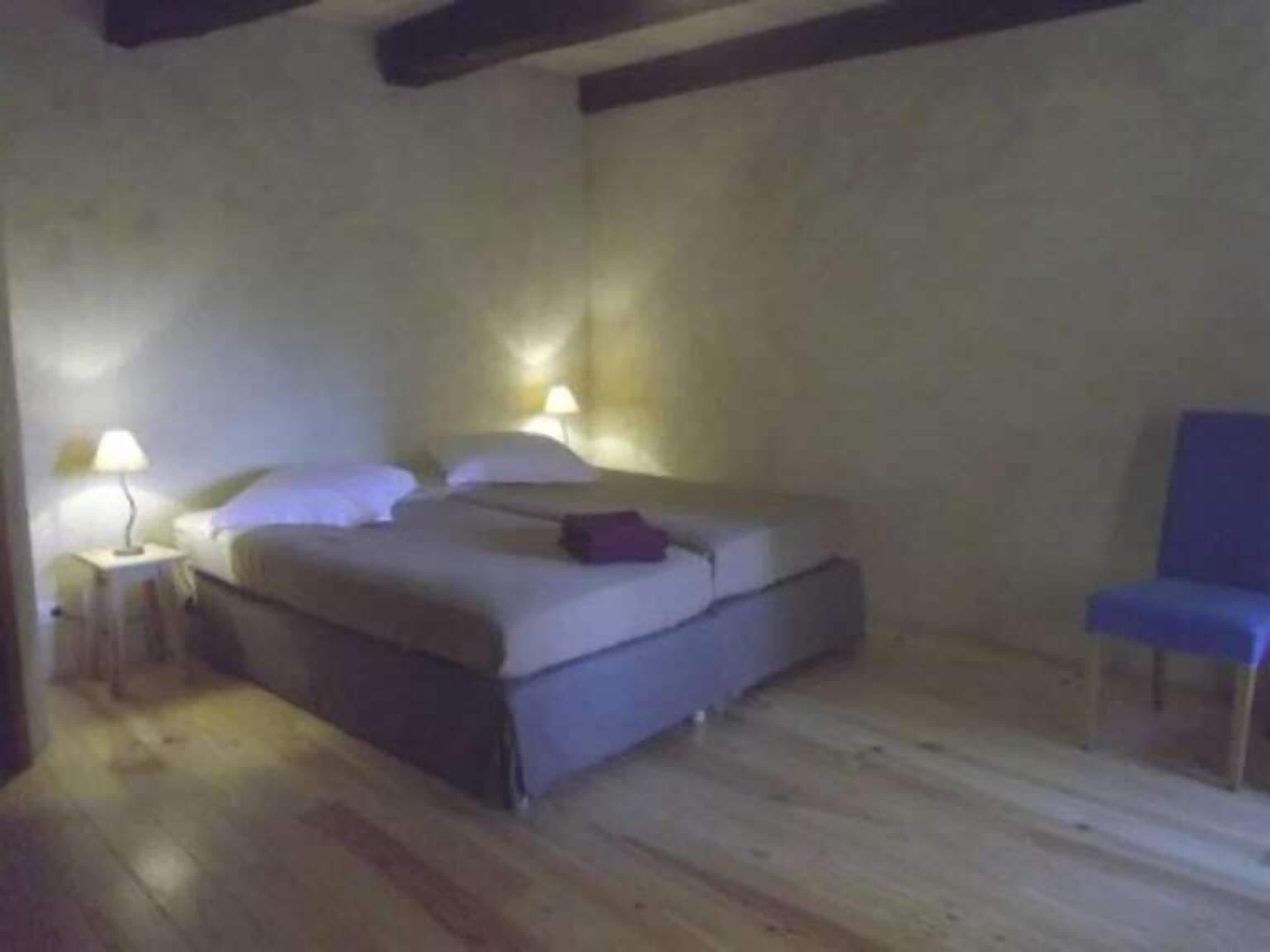 Un dormitorio con cama, dos lámparas de noche, una silla y suelo de madera.