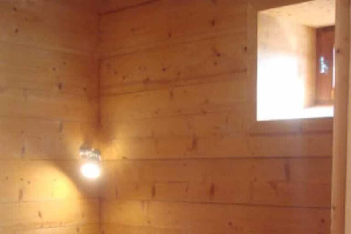 A small, single-room cabin with a bed, a window, and a wall-mounted light fixture.
