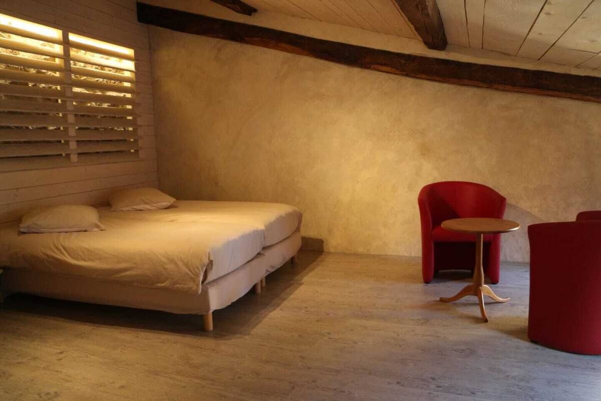 A bedroom with a bed, a red chair, and a small round table.