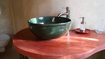 Un évier en céramique verte, doté d’un robinet moderne et d’un distributeur de savon, est installé sur un plan de toilette en cuivre dans une salle de bain.