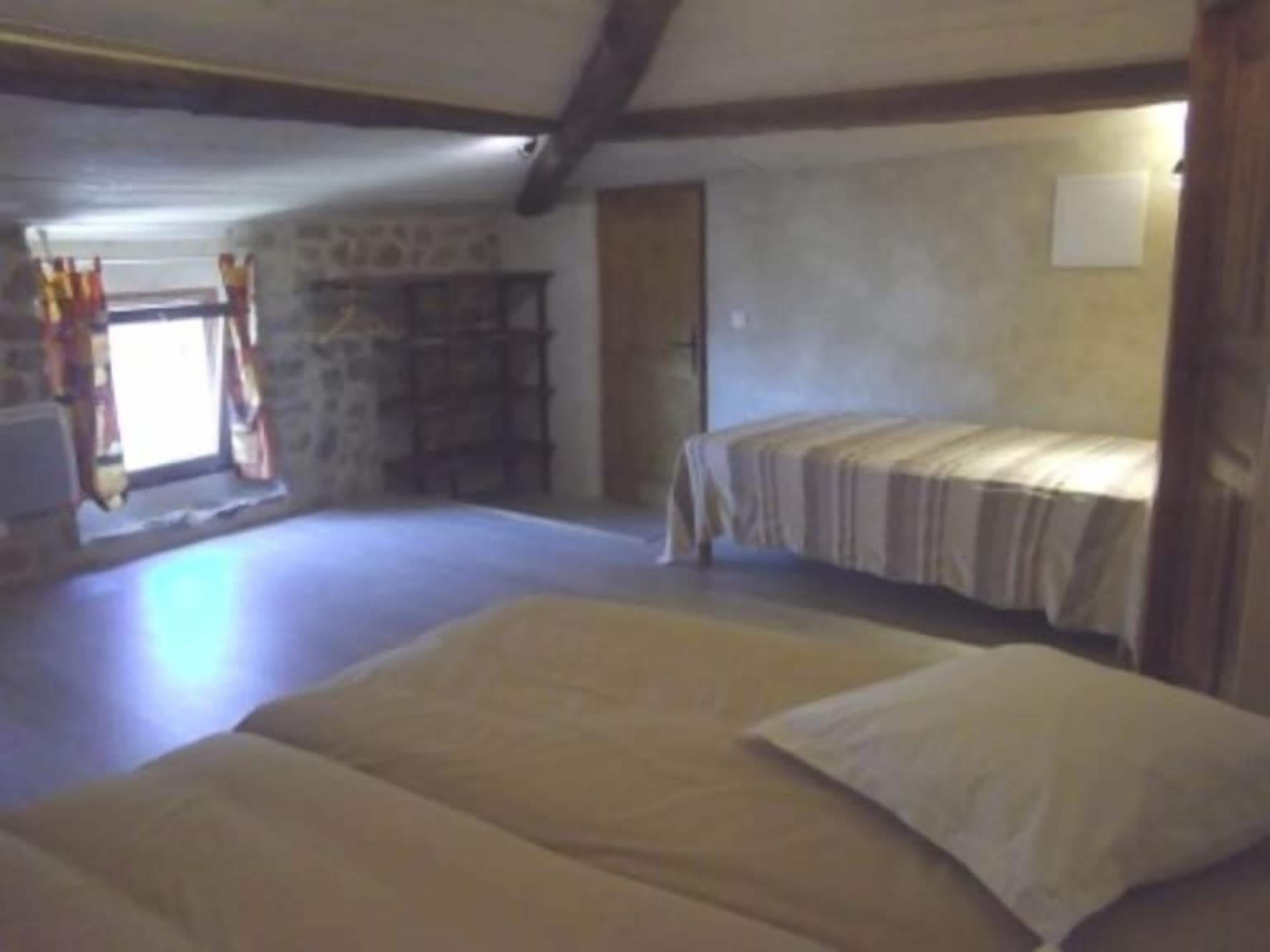 Une chambre avec deux lits, un mur en pierre et une fenêtre avec des rideaux.