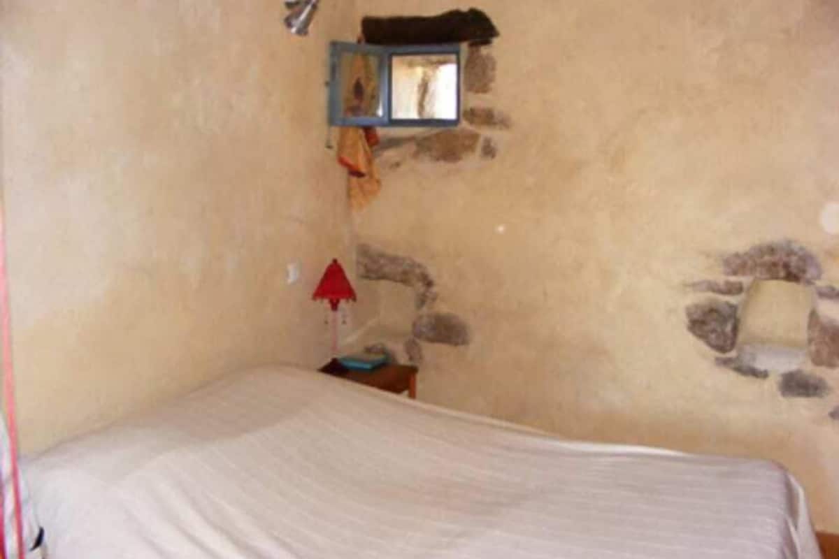 A small, rustic room with a single bed, a small table, and a stone wall.