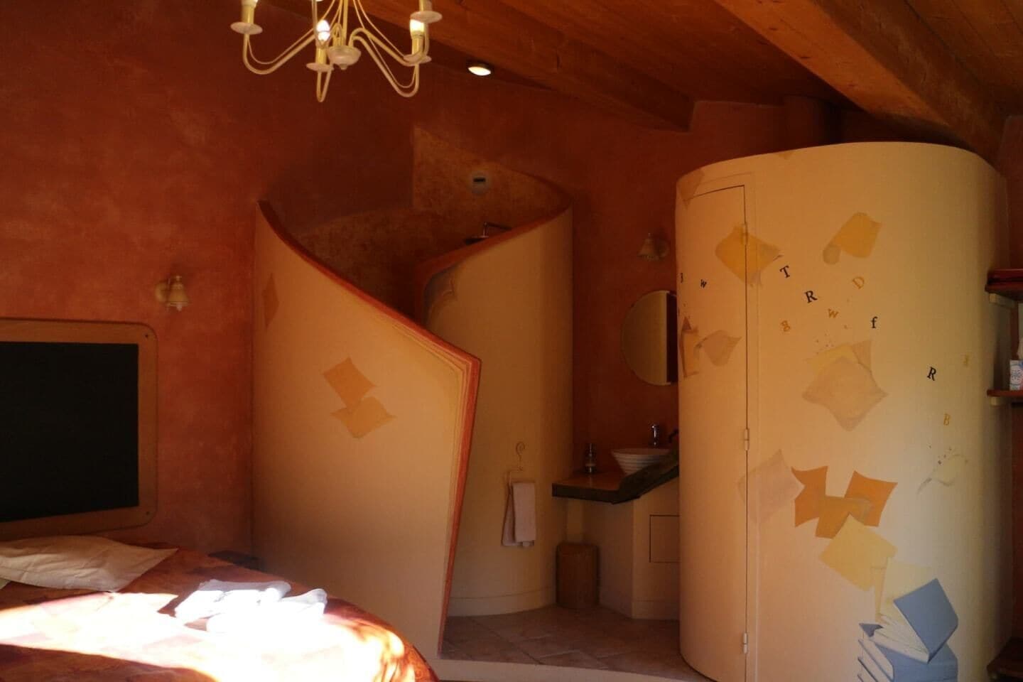 Ein Schlafzimmer mit einem Bett, einem gewölbten weißen Schrank, einem kleinen Waschbecken und einer Chandelieber.