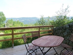 Enjoy outdoor dining or relaxation on this deck overlooking a serene landscape with trees and distant hills.