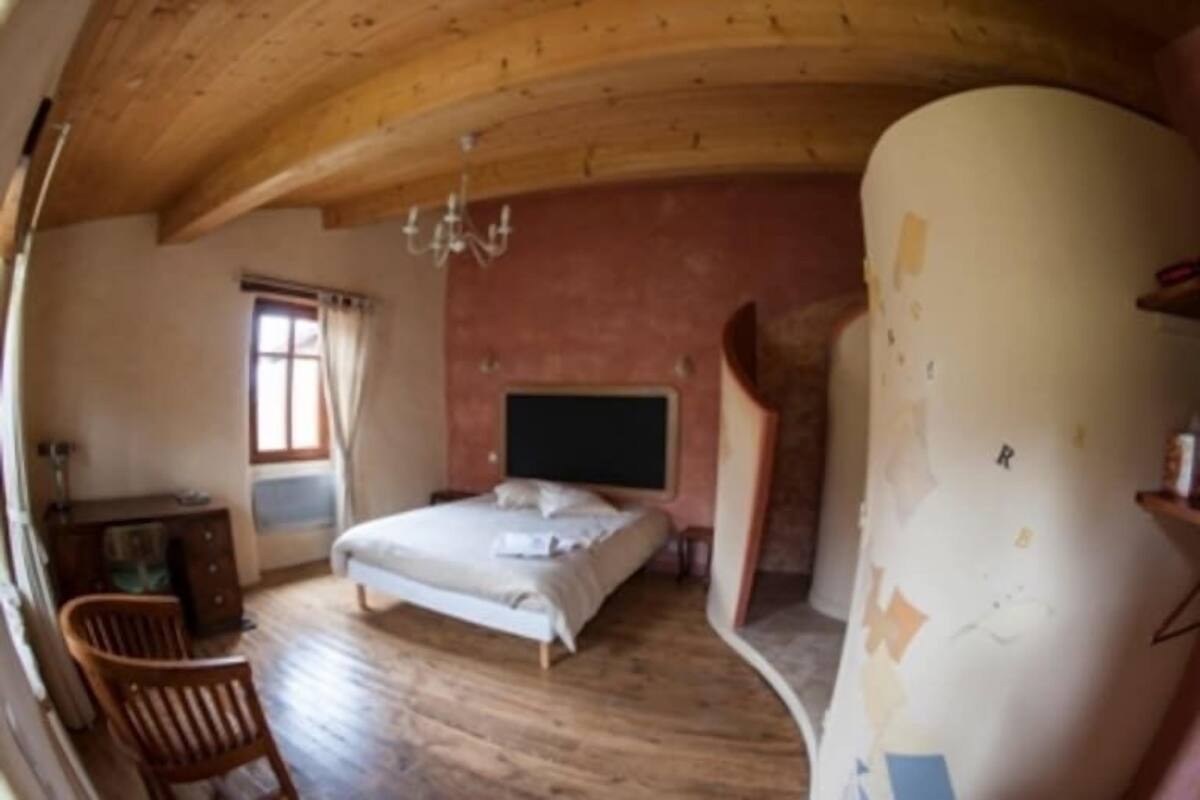 A bedroom with a wooden ceiling, a bed, a desk, and a window.