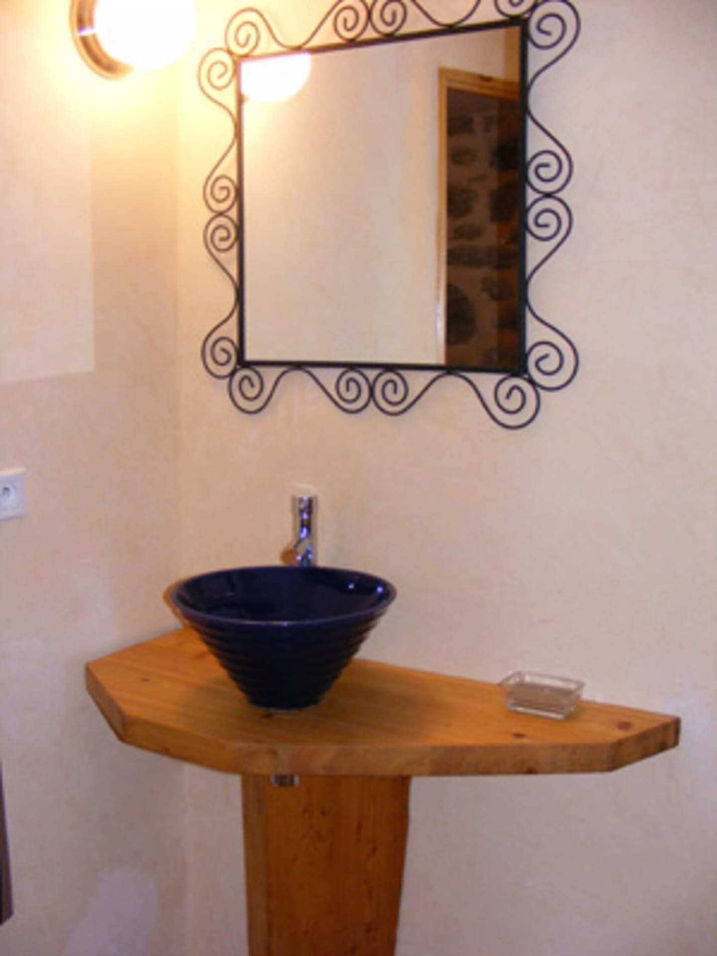 A bathroom with a wooden vanity, a blue vessel sink, and a wall-mounted mirror with a decorative frame.