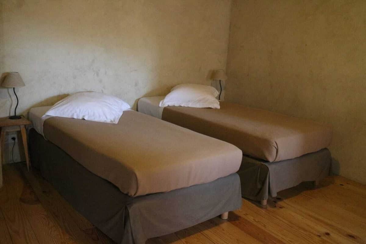 A room with two single beds, each with a pillow and a lamp on a side table.