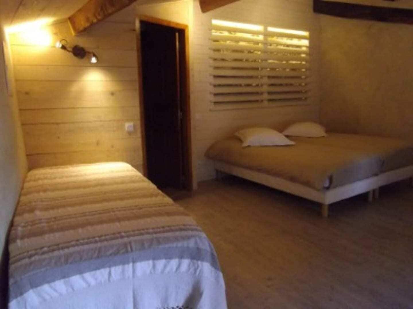 Une petite pièce agréable, dotée d’un lit simple et d’un lit plus petit, de murs en bois et d’une fenêtre avec des stores.