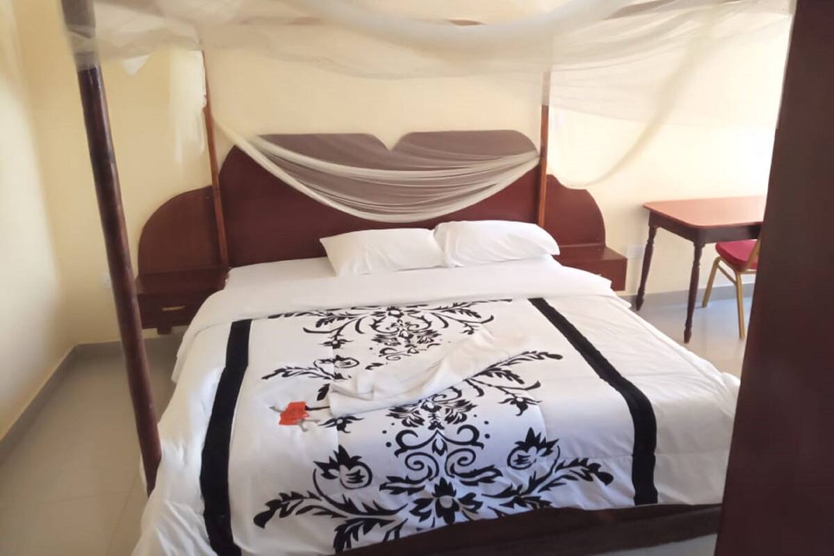 A bed with a canopy, a wooden headboard, and a table with a chair in the room.