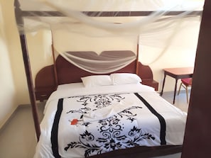 A bed with a canopy, a wooden headboard, and a table with a chair in the room. - Drimz Hotel Busia (Busia)