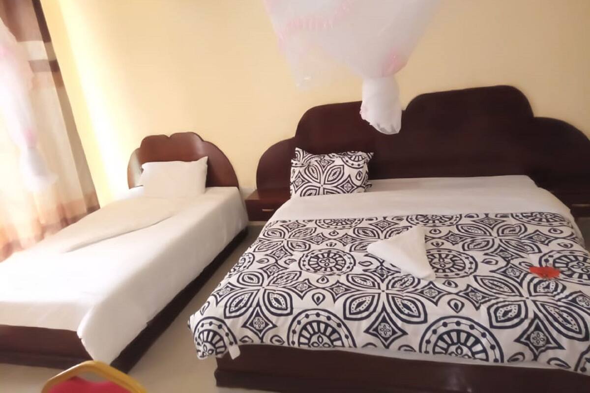 A hotel room with two beds, one with a patterned bedspread and the other with plain sheets.