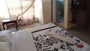 A bedroom with a four-poster bed, a desk with a chair, a television, and a bathroom visible through a glass partition. - Drimz Hotel Busia (Busia)