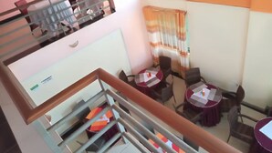 A dining area with tables and chairs, a staircase, and a window with curtains. - Drimz Hotel Busia (Busia)
