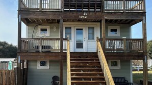 Ein zweistöckiges Haus mit einer Holzterrasse und einer Treppe, die zum zweiten Stock führt.