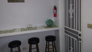 A kitchen with a white countertop, three stools, a fire extinguisher, and a decorative door. - Hillside Breeze (Nassau)