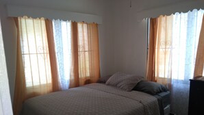 A bedroom with a bed, curtains, and a dresser. - Hillside Breeze (Nassau)