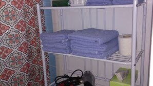 A bathroom with a metal shelf holding towels, a hairdryer, and toiletries. - Hillside Breeze (Nassau)