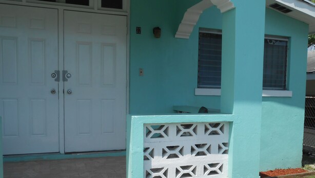 A house with a turquoise exterior, white doors, and a small porch area. - Hillside Breeze (Nassau)