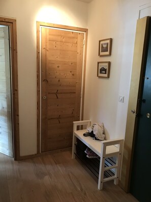 Eine Holztür mit Leuchte darüber, eine kleine Bank mit Tasche und Schuhen, sowie zwei gerahmte Bilder an der Wand.