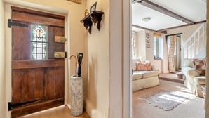 Un hall d’entrée accueillant, avec une porte en bois, un porte-parapluie décoratif et un escalier menant à un espace de vie comprenant un canapé et des coussins.