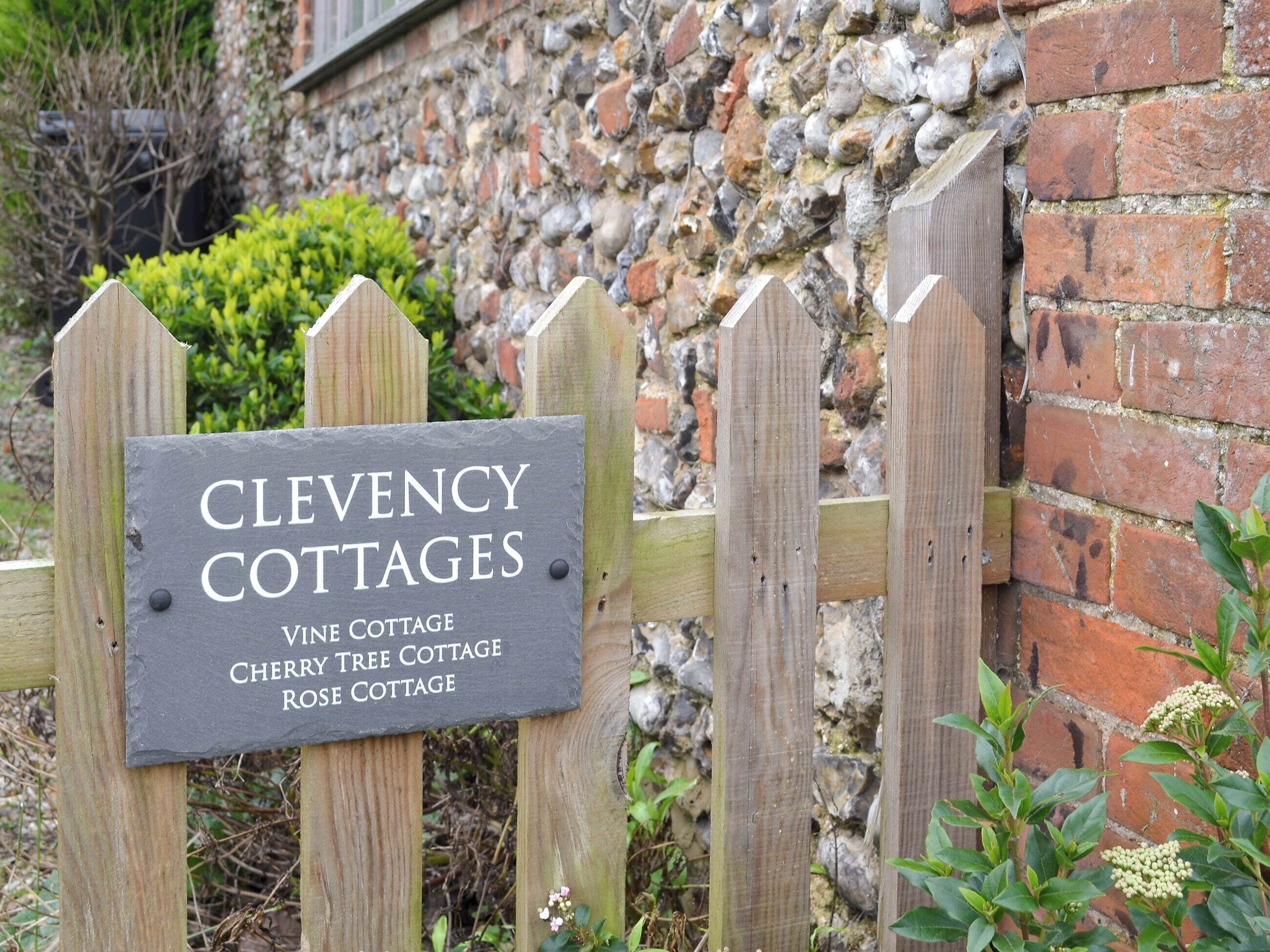 Ein hölzernes Schild mit dem Schriftzug 'Clevency Cottages' und den Namen verschiedener Ferienhäuser.