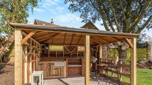 Une structure de cuisine extérieure en bois, dotée d’un comptoir en briques, d’un évier et d’un espace repas avec des chaises.