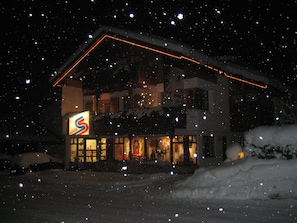 A snow-covered building with a lit sign, surrounded by falling snowflakes. - AlpinAppartements Stöckl (Gaschurn)