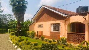 A two-story house with a tiled roof, a water tank on the roof, and a well-maintained garden with hedges and a palm tree. - Watercrest Gardens (Eldoret)