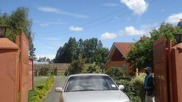 A residential street with a parked car, a person standing by a gate, and houses with red roofs.