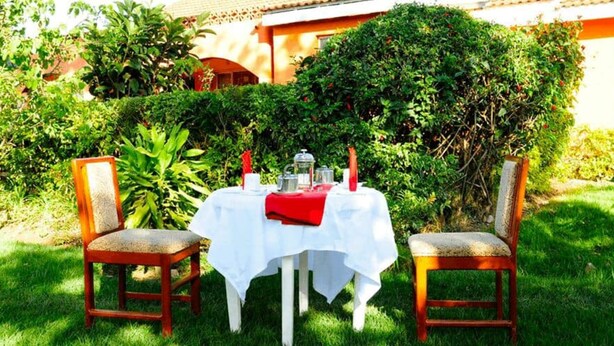 A table set outdoors with a white tablecloth, two wooden chairs, and a red cloth. - Watercrest Gardens (Eldoret)