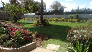 A well-maintained garden with a variety of plants and flowers, a grassy lawn, and a stone bench. - Watercrest Gardens (Eldoret)