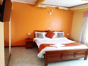 A bedroom with a wooden bed, orange walls, and a small nightstand. - Watercrest Gardens (Eldoret)
