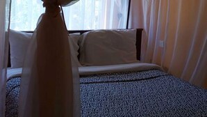 A bed with a canopy, a patterned bedspread, and a window with curtains. - Watercrest Gardens (Eldoret)