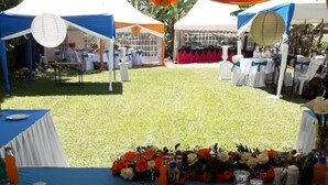 A tented outdoor event area with tables set for a meal, featuring white and blue tablecloths and a floral centerpiece. - Watercrest Gardens (Eldoret)