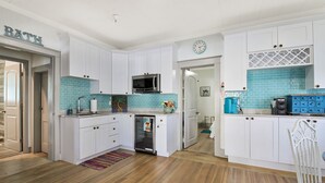 Una cocina con armarios blancos, microondas, refrigerador y un reloj en la pared.