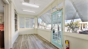 Un pasillo amplio con piso de madera, ventanas grandes y una puerta verde azulado.