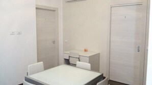 A small, clean room with a white table and chairs, a desk with a chair, and two doors. - La Perla Del Sole (Corigliano-Rossano)