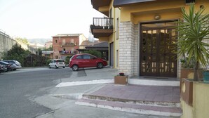 A residential building with a gated entrance, a red car parked in front, and a small garden area with a potted plant. - La Perla Del Sole (Corigliano-Rossano)