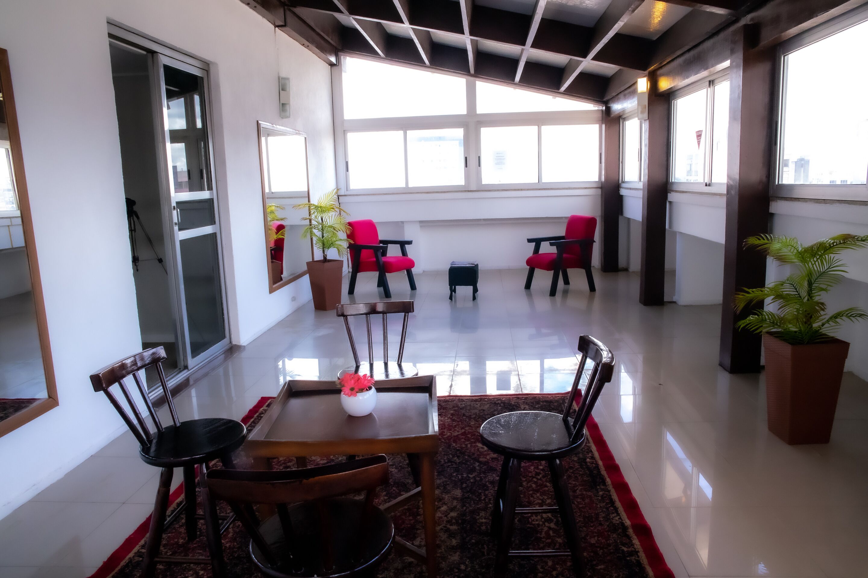 A spacious room with a high ceiling, large windows, and a central table with chairs.