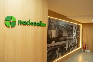 A wooden reception desk with a 'nacionalhm' logo and a wall-mounted photo display. - Hotel Nacional Inn Porto Alegre (Porto Alegre)