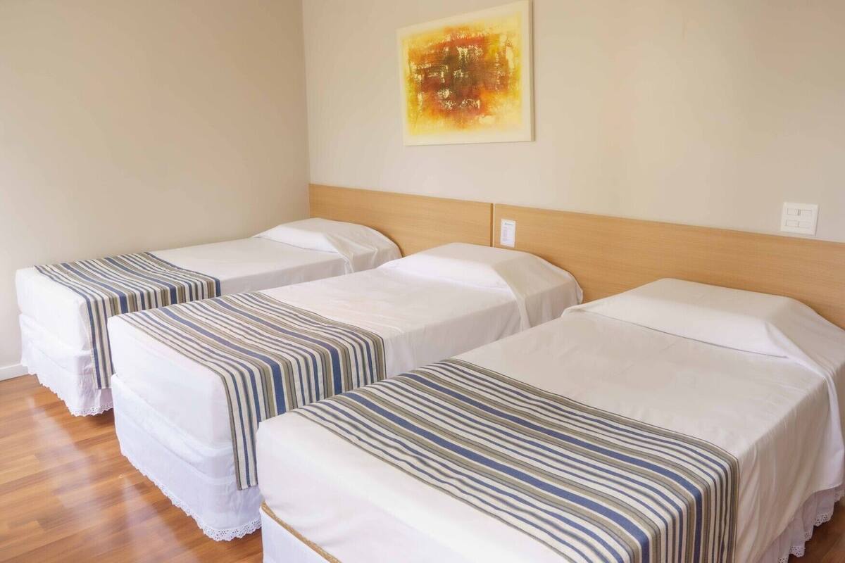 A hotel room with three single beds, each with a striped bedspread.