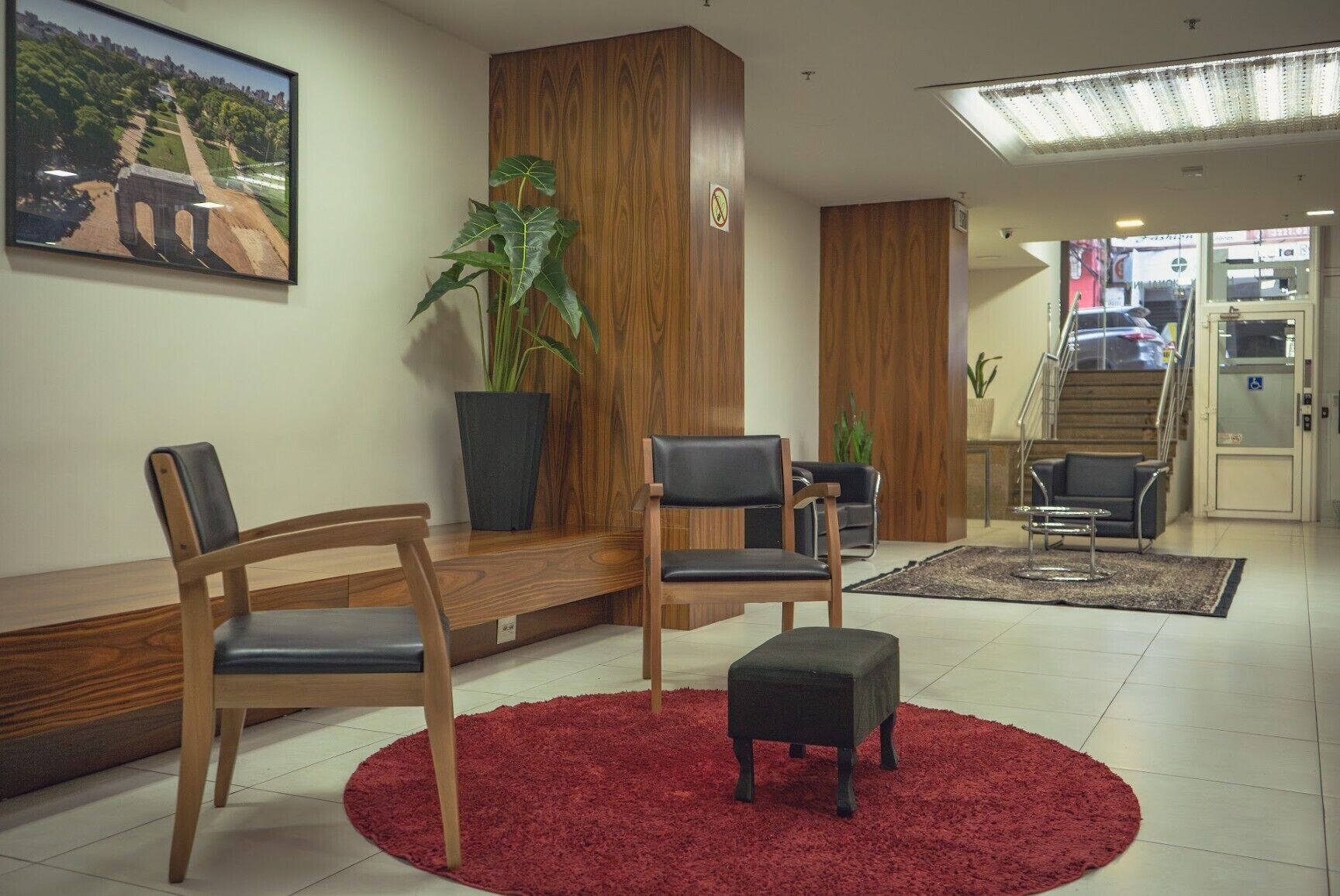 A reception area with wooden furniture, a red rug, and a large potted plant.